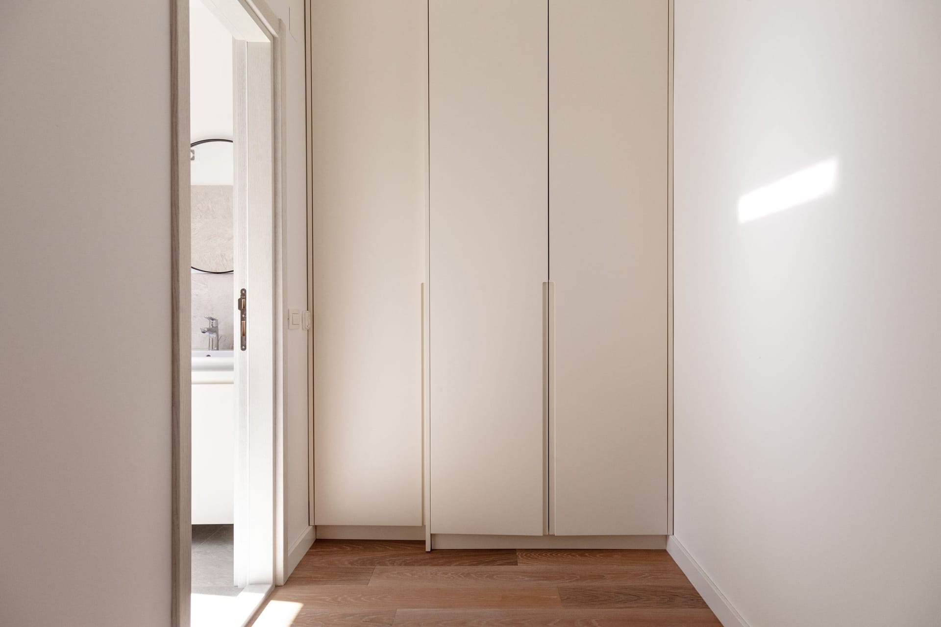 Built-in light-colored closet in the hallway of a modern apartment in Kotor, Montenegro, with a view of the bathroom.