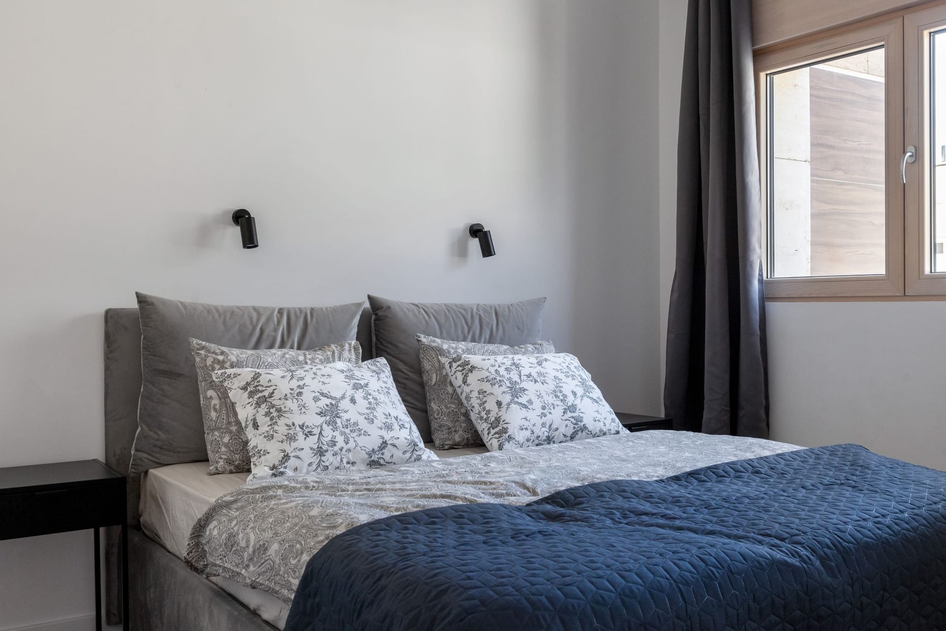 Modern bedroom with a double bed in an apartment in Kotor, Montenegro: gray textiles and stylish wall lamps.