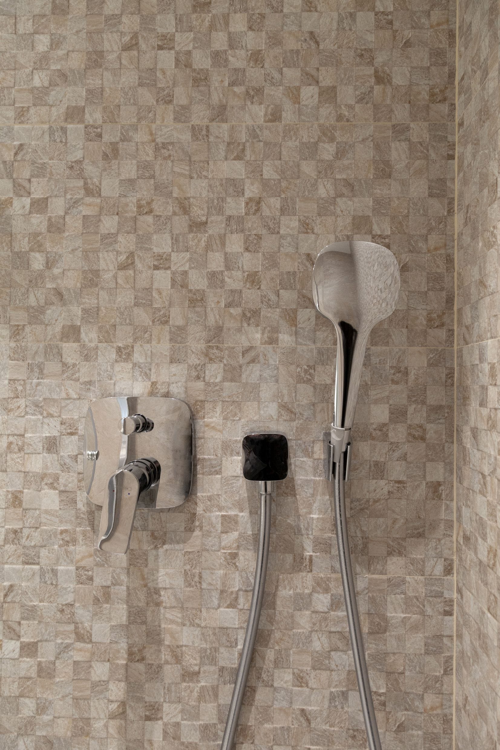 Modern showerhead and faucet against beige mosaic tiles in the bathroom of an apartment in Kotor, Montenegro.