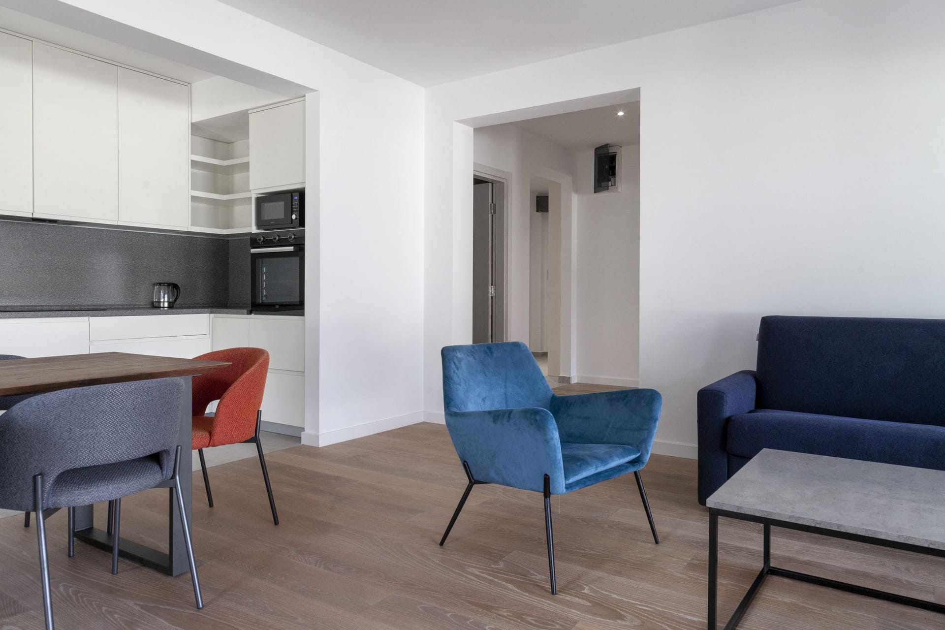Modern living room with kitchen in an apartment in Kotor, Montenegro: blue armchairs, dining area, and light finishes.