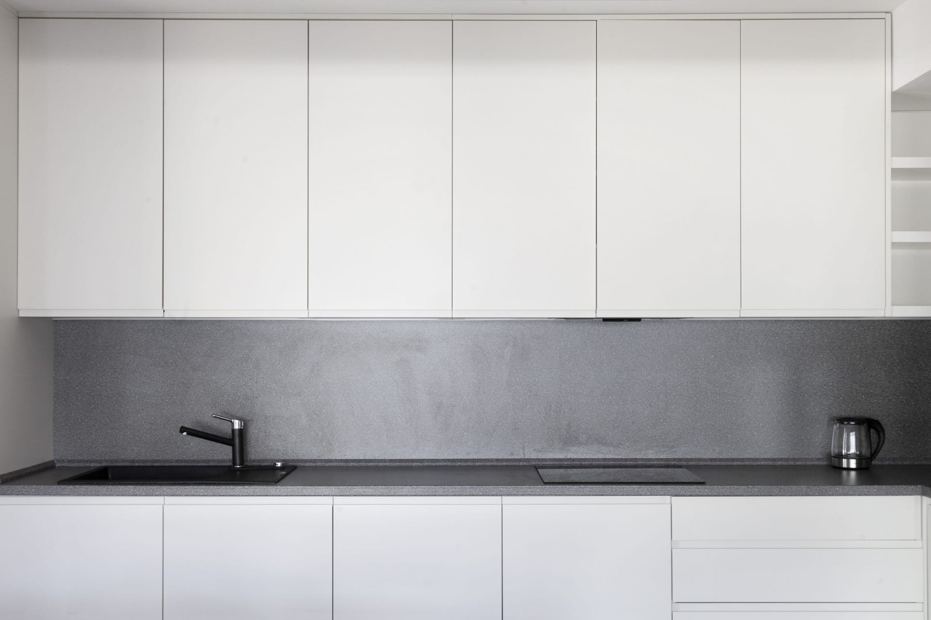 Modern white kitchen with a gray backsplash in an apartment for sale, Kotor, Montenegro. Built-in appliances and sink.