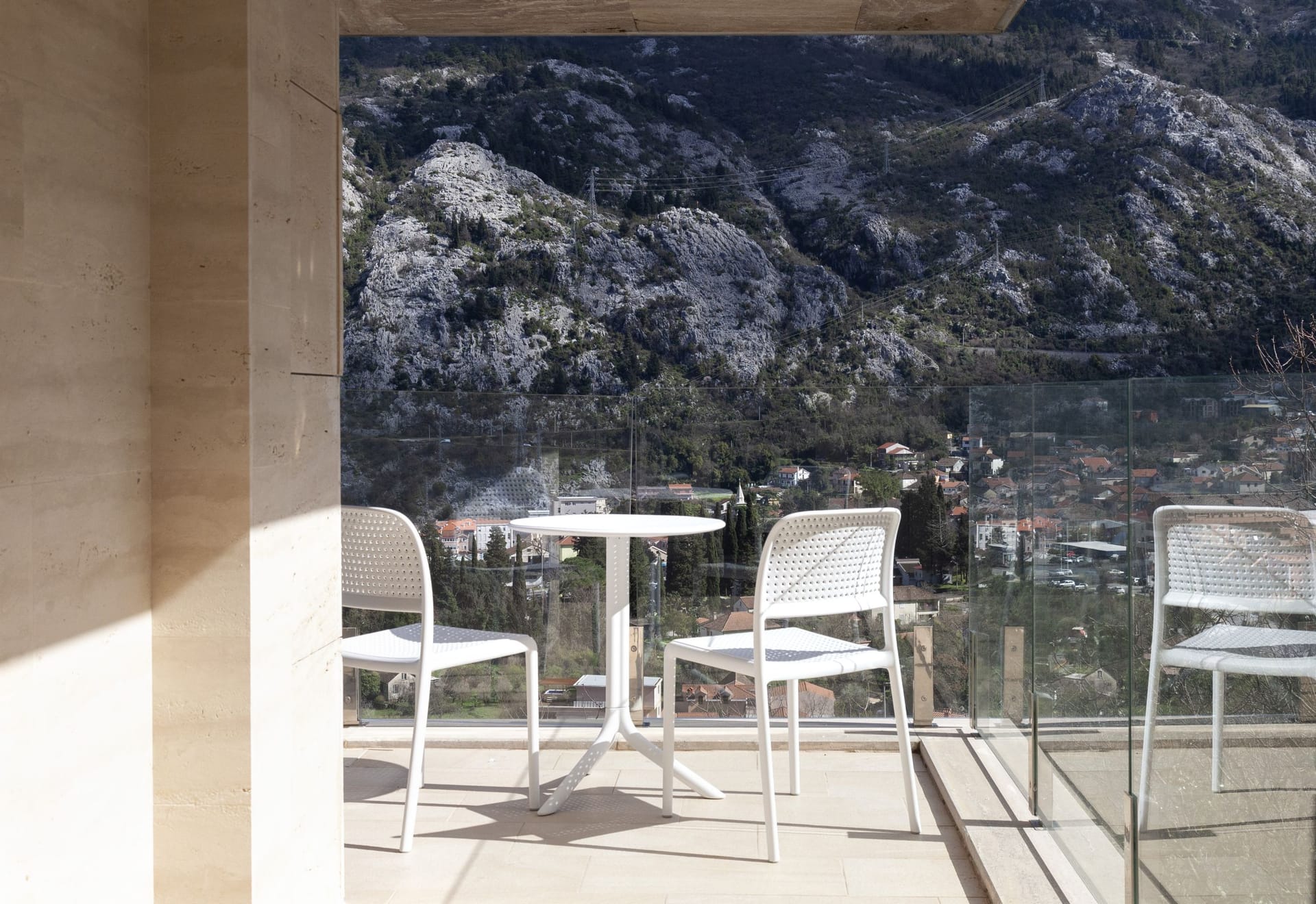 Balcony with white furniture and panoramic views of the mountains and the city of Kotor, Montenegro. Modern finishes and glass railing.