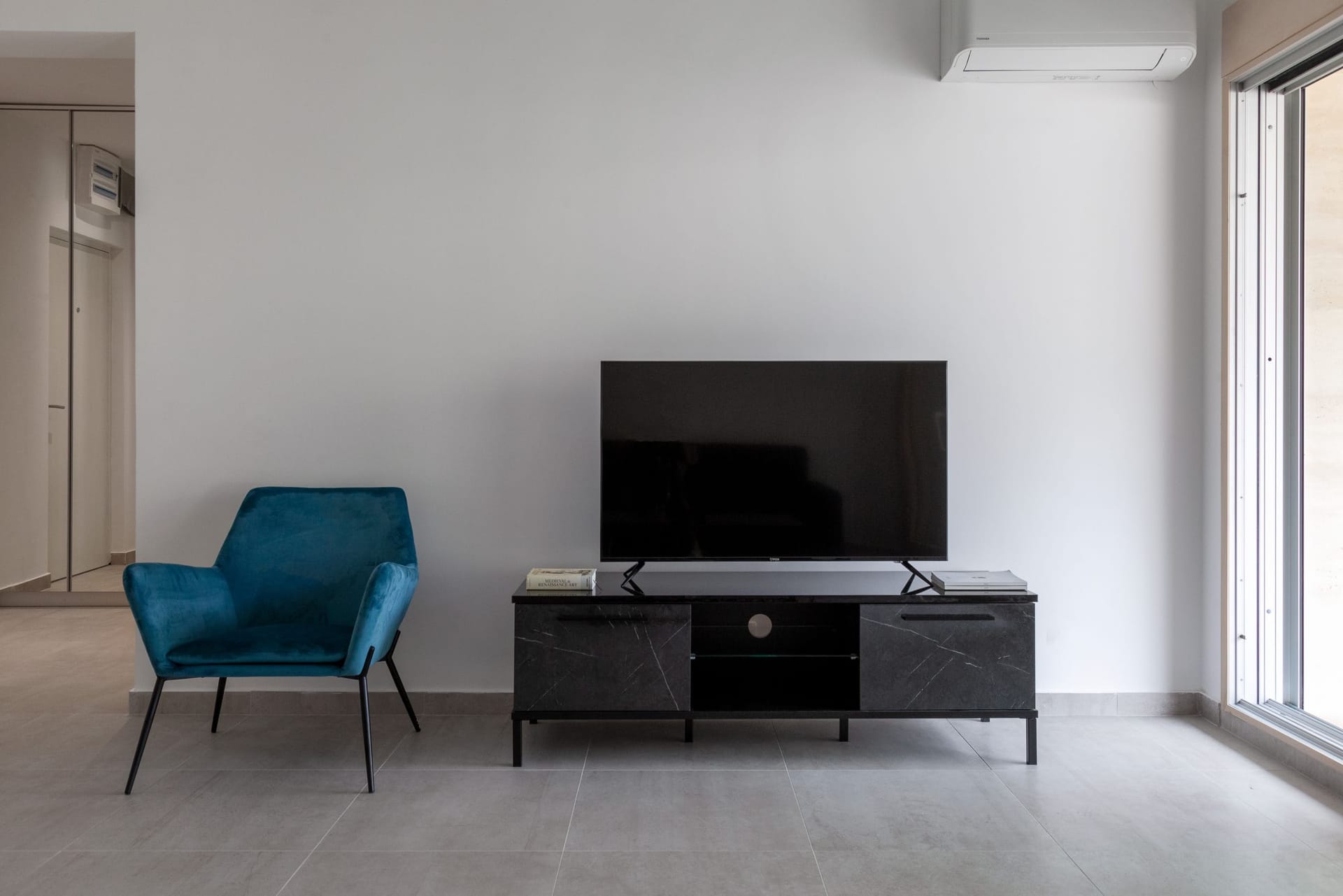 Modern living room in an apartment in Kotor, Montenegro: blue armchair, black TV stand, and panoramic window.