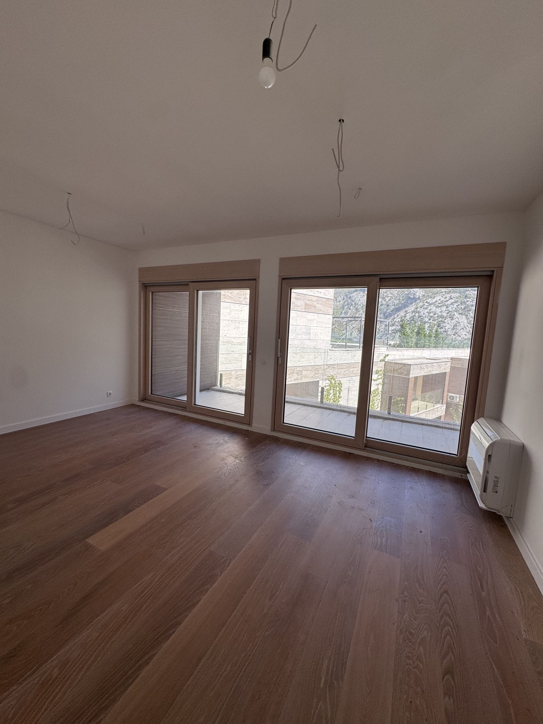 Bright living room with parquet flooring and panoramic windows in a new apartment in Kotor, Montenegro, with mountain and terrace views.