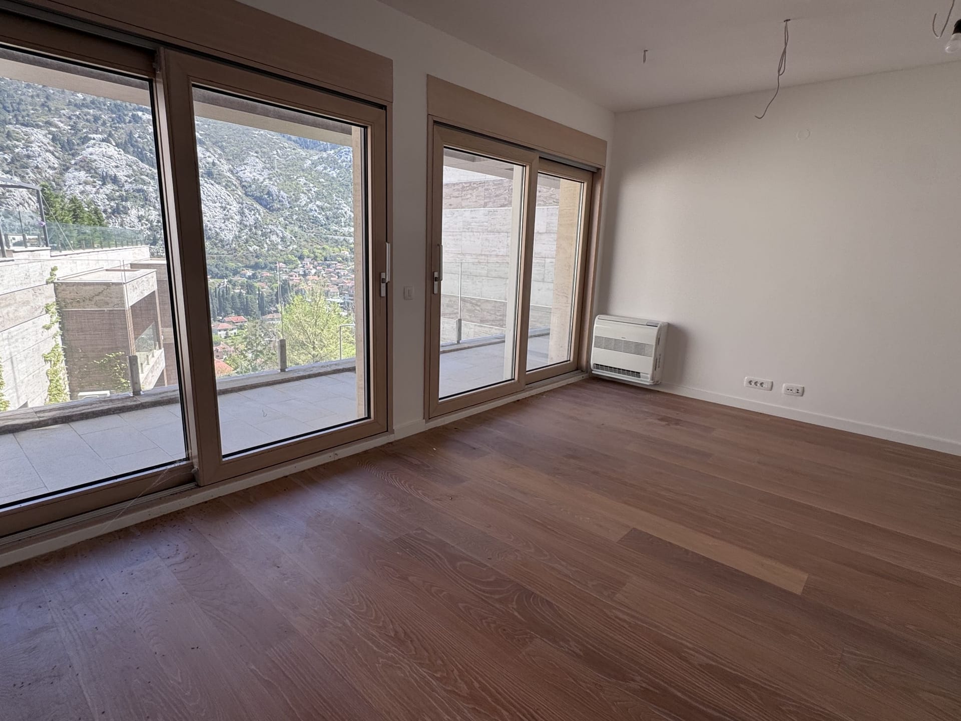 Bright living room in an apartment in Kotor, Montenegro: panoramic windows, mountain view, parquet floor, and access to the terrace.