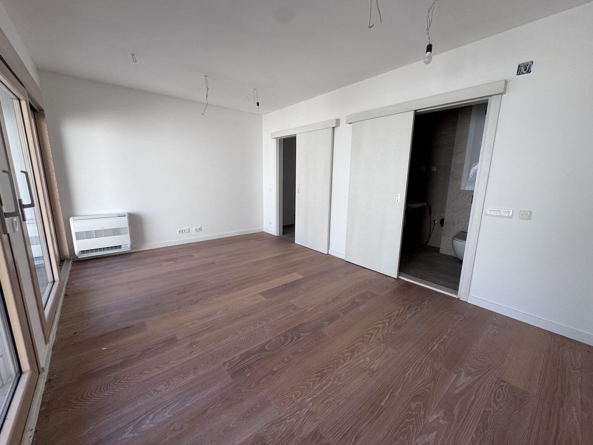 Bright bedroom in a new apartment in Kotor, Montenegro: parquet flooring, sliding doors, and access to the balcony.