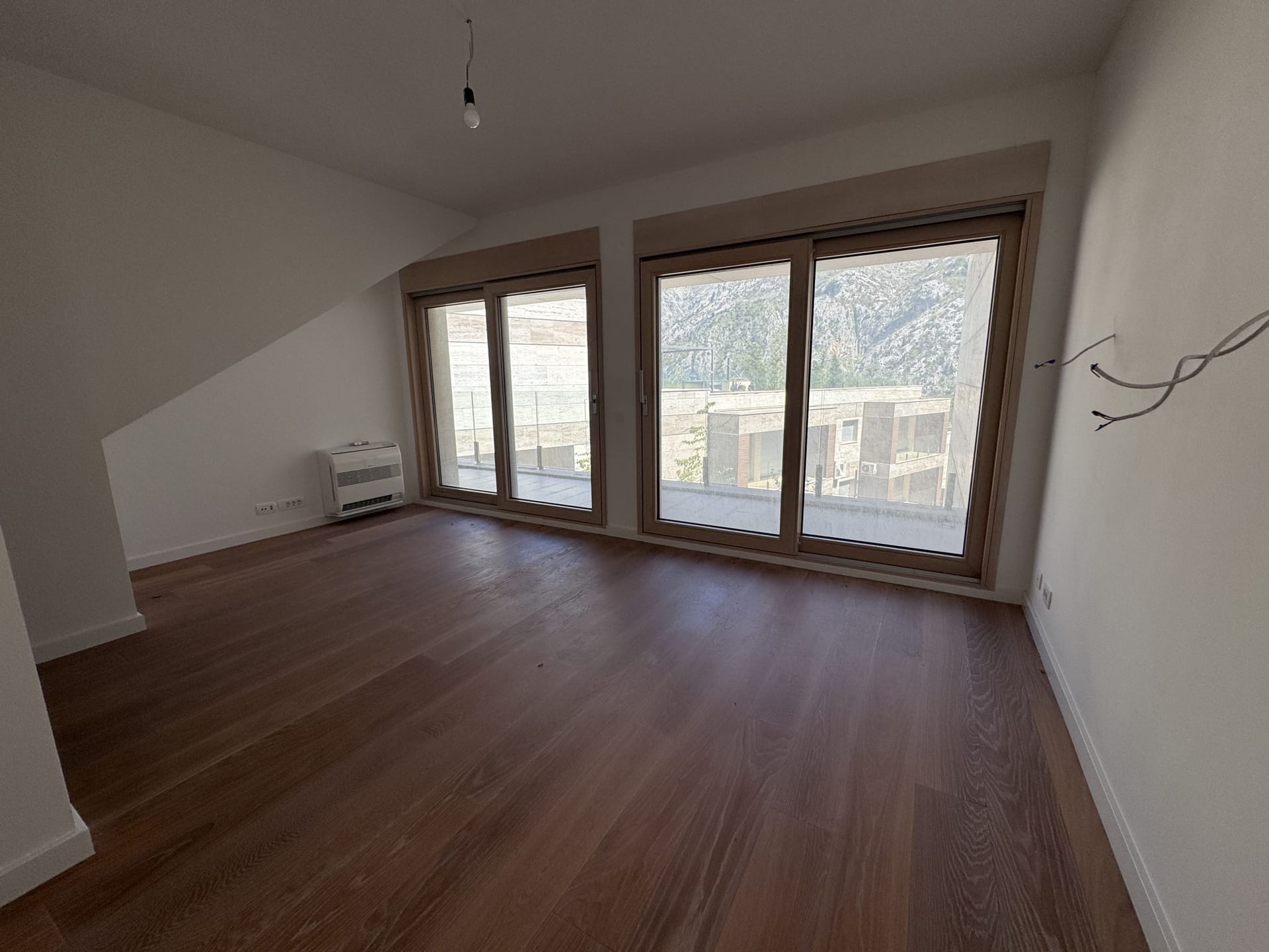 Bright living room in a new building in Kotor, Montenegro: panoramic windows, mountain view, parquet flooring, and access to the terrace.