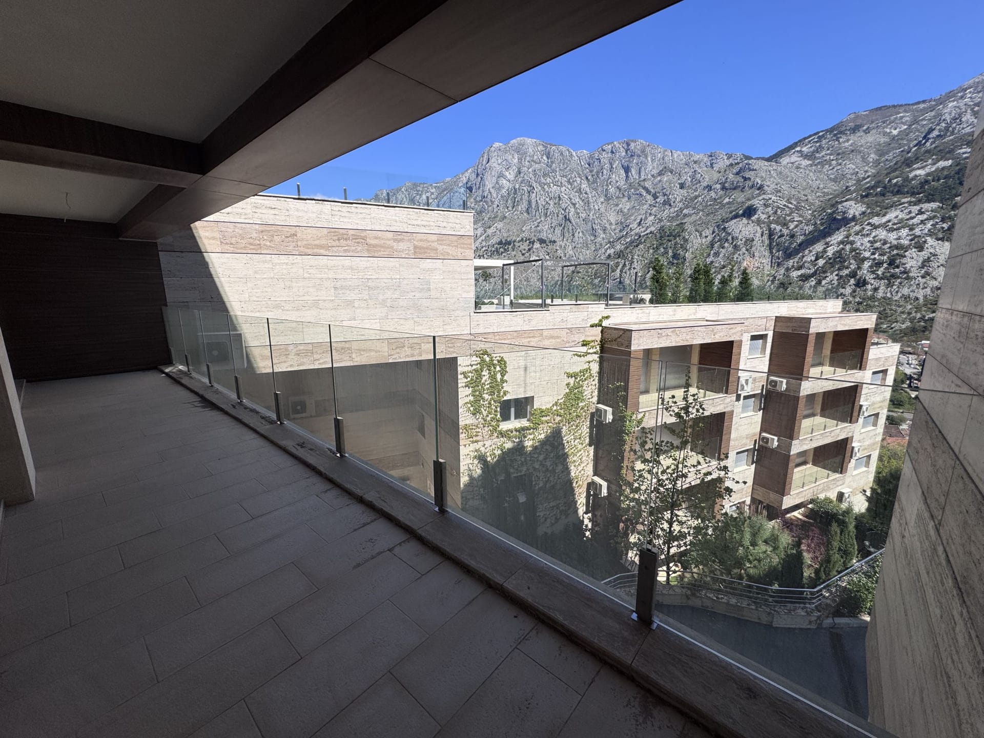 Spacious terrace with panoramic mountain views in a modern apartment, Kotor, Montenegro. Stone and glass finishes.