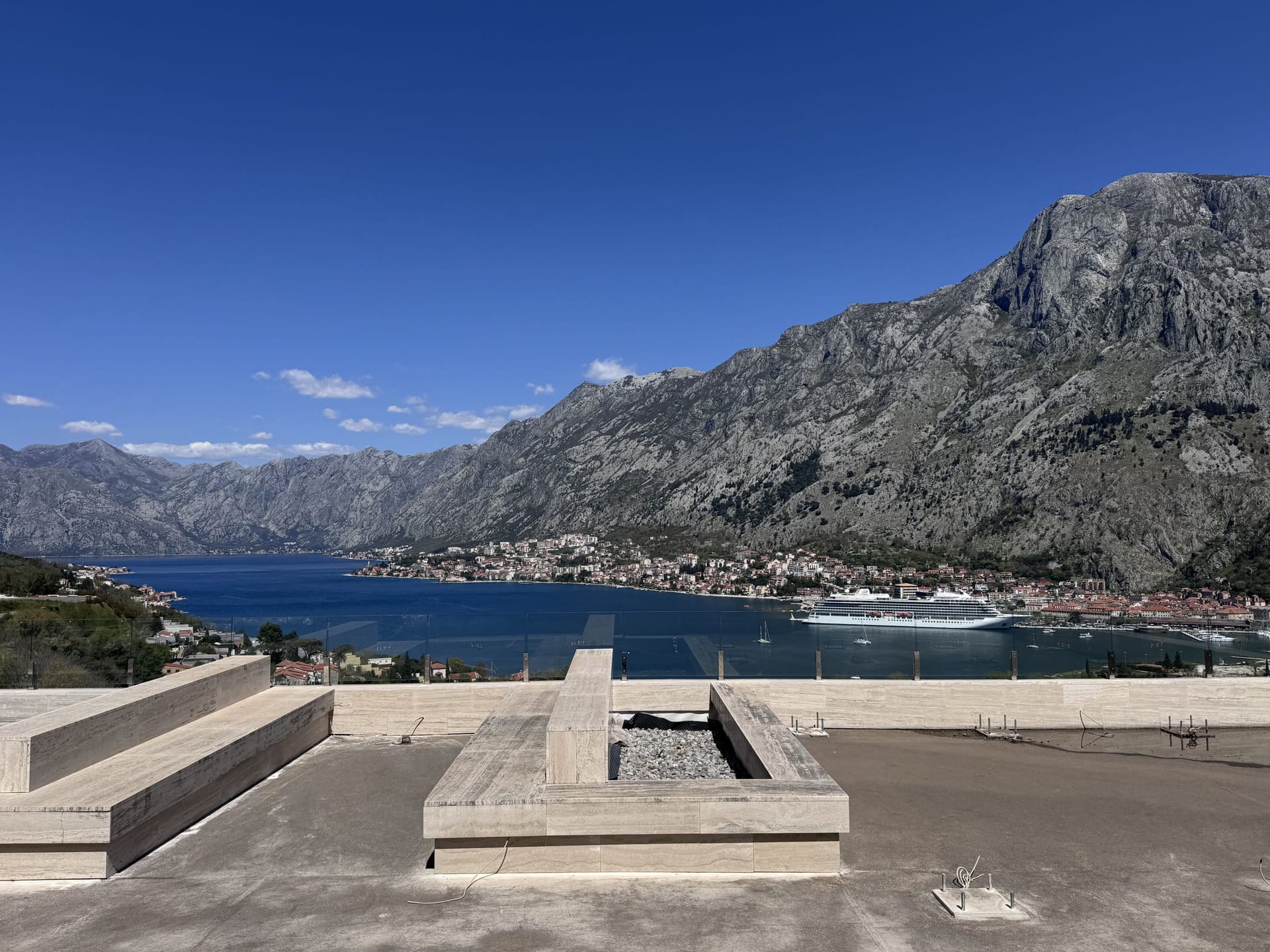 Panoramic view of the Bay of Kotor and the mountains from the apartment terrace in Kotor, Montenegro, with a stone seating area.