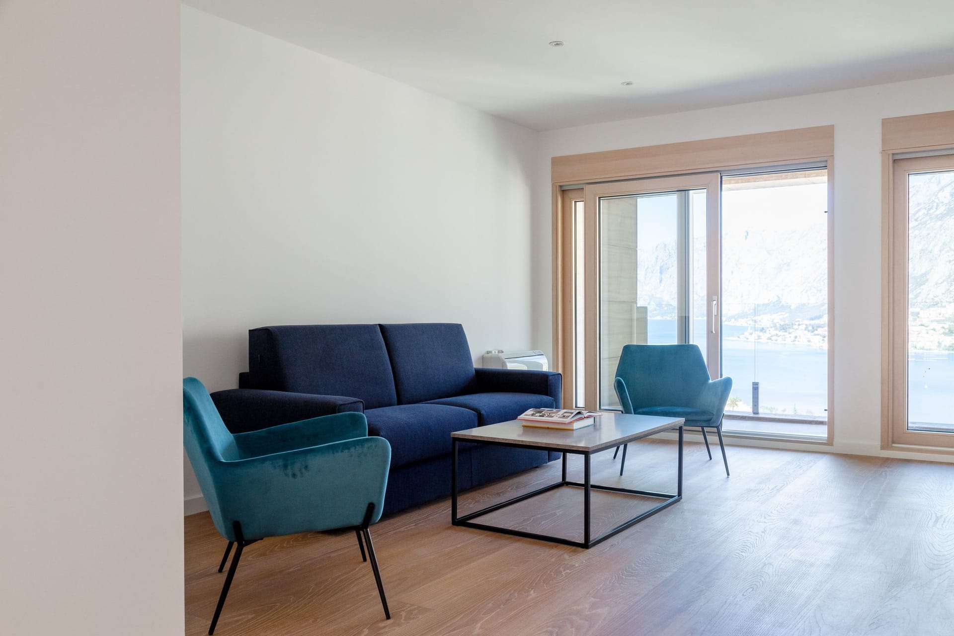 Modern living room in an apartment in Kotor, Montenegro: blue sofa, armchairs, panoramic view of Kotor Bay and the mountains.