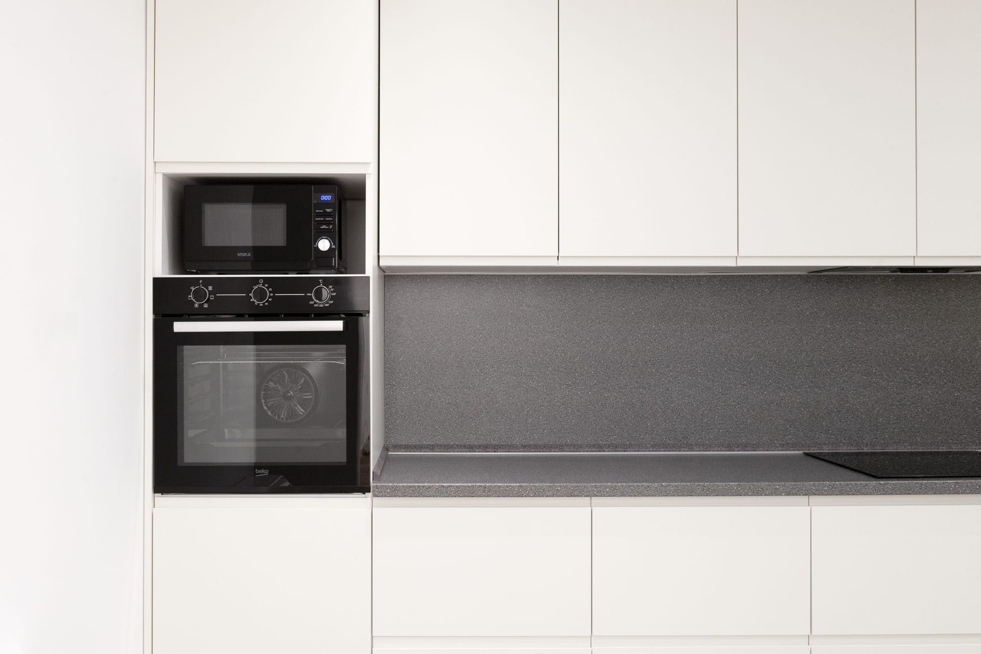 Modern white kitchen with a gray countertop and built-in Beko appliances in an apartment in Kotor, Montenegro.