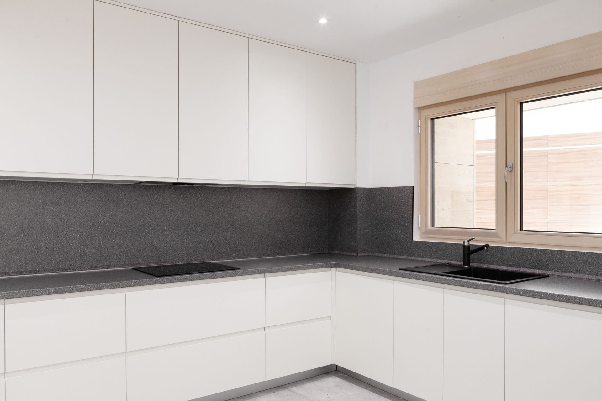 Modern white kitchen with a dark countertop in an apartment, Kotor, Montenegro: built-in appliances and a bright window.