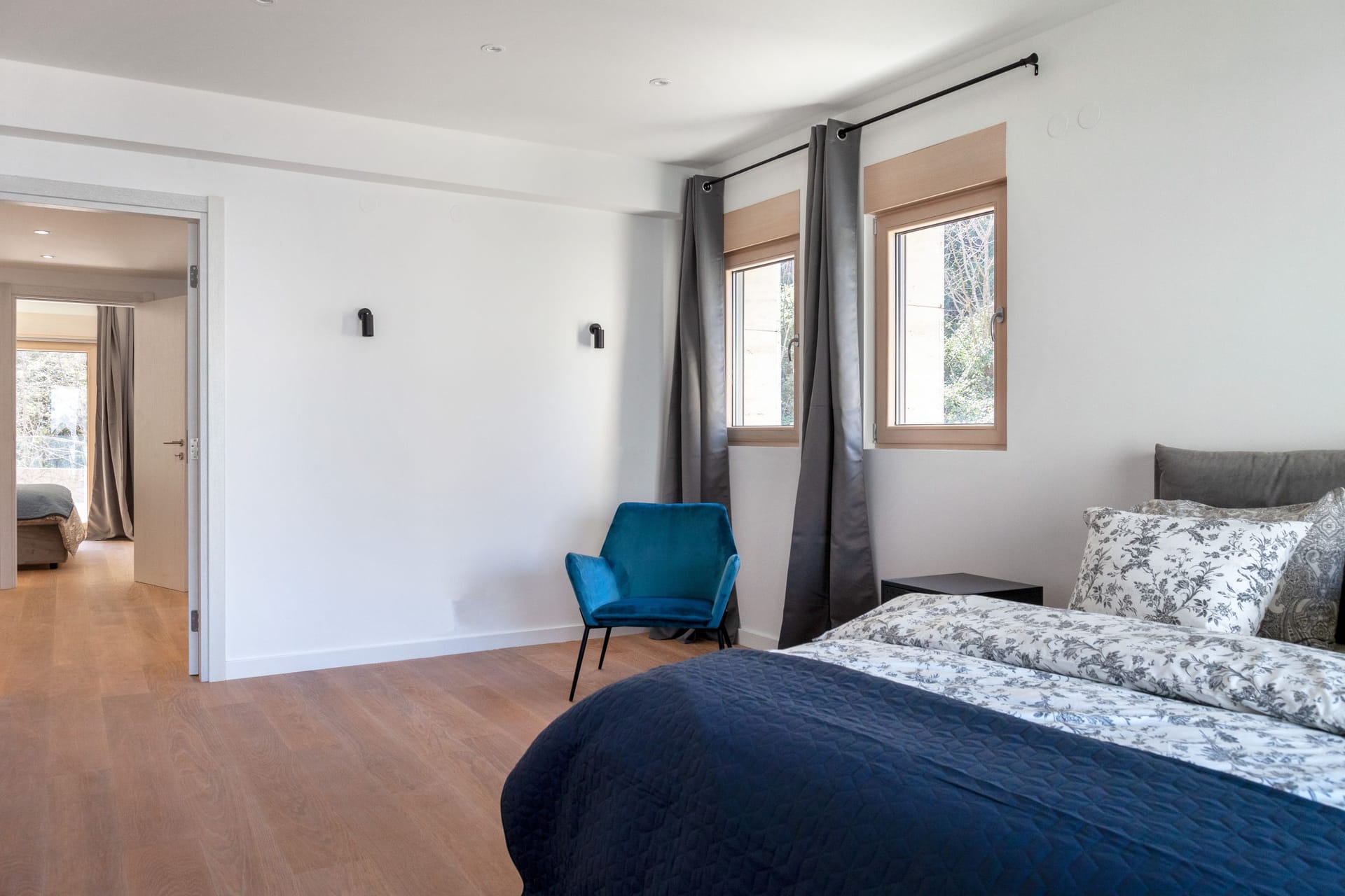 Modern bedroom in an apartment in Kotor, Montenegro: blue armchair, double bed, light parquet flooring, and a view from the window.