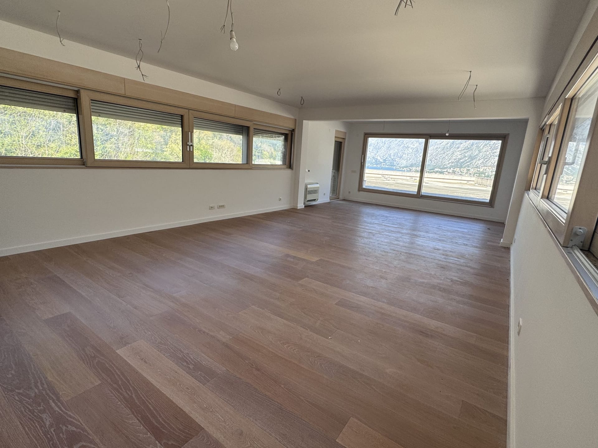Spacious living room in a duplex in Kotor, Montenegro: panoramic windows, mountain view, and wooden flooring, unfurnished.