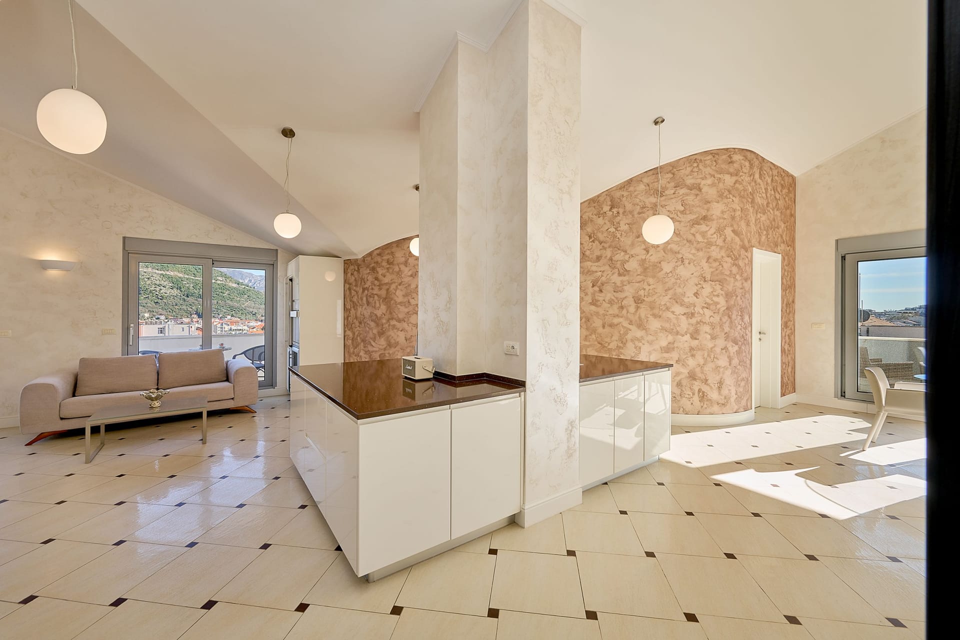 Modern kitchen-living room in an apartment in Budva, Montenegro: glossy fronts, decorative plaster, and mountain views.