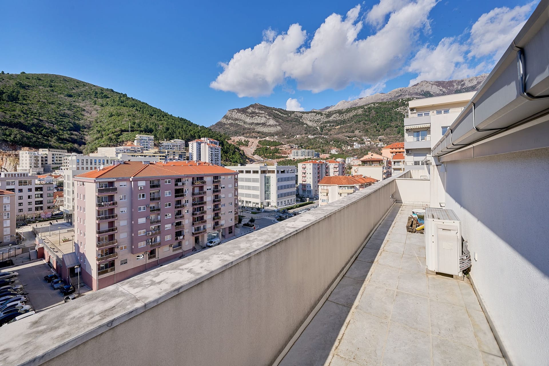 Spacious apartment balcony in Budva, Montenegro, with panoramic views of the city buildings and mountain scenery.