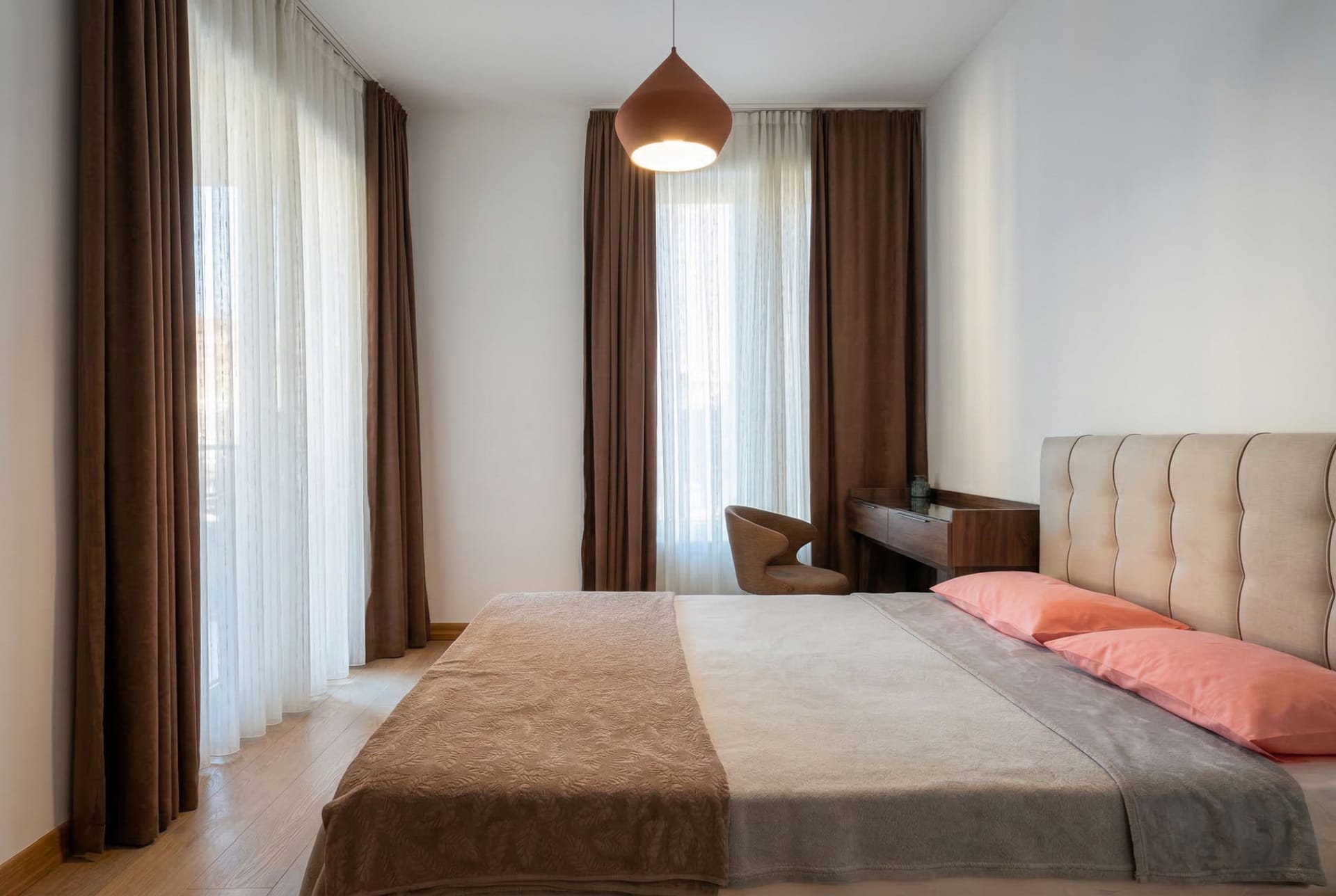 Modern bedroom in an apartment in Budva, Montenegro: a double bed, vanity table, and panoramic windows with curtains.