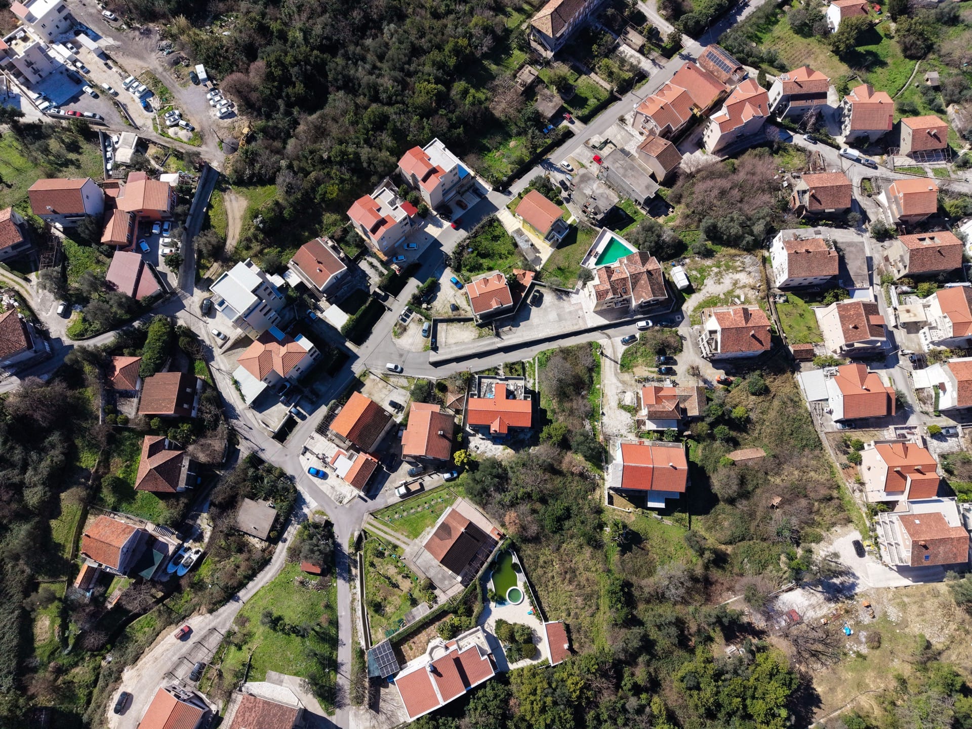 Aerial view of a residential area in Tivat, Montenegro: private houses with red roofs, green plots, and roads.