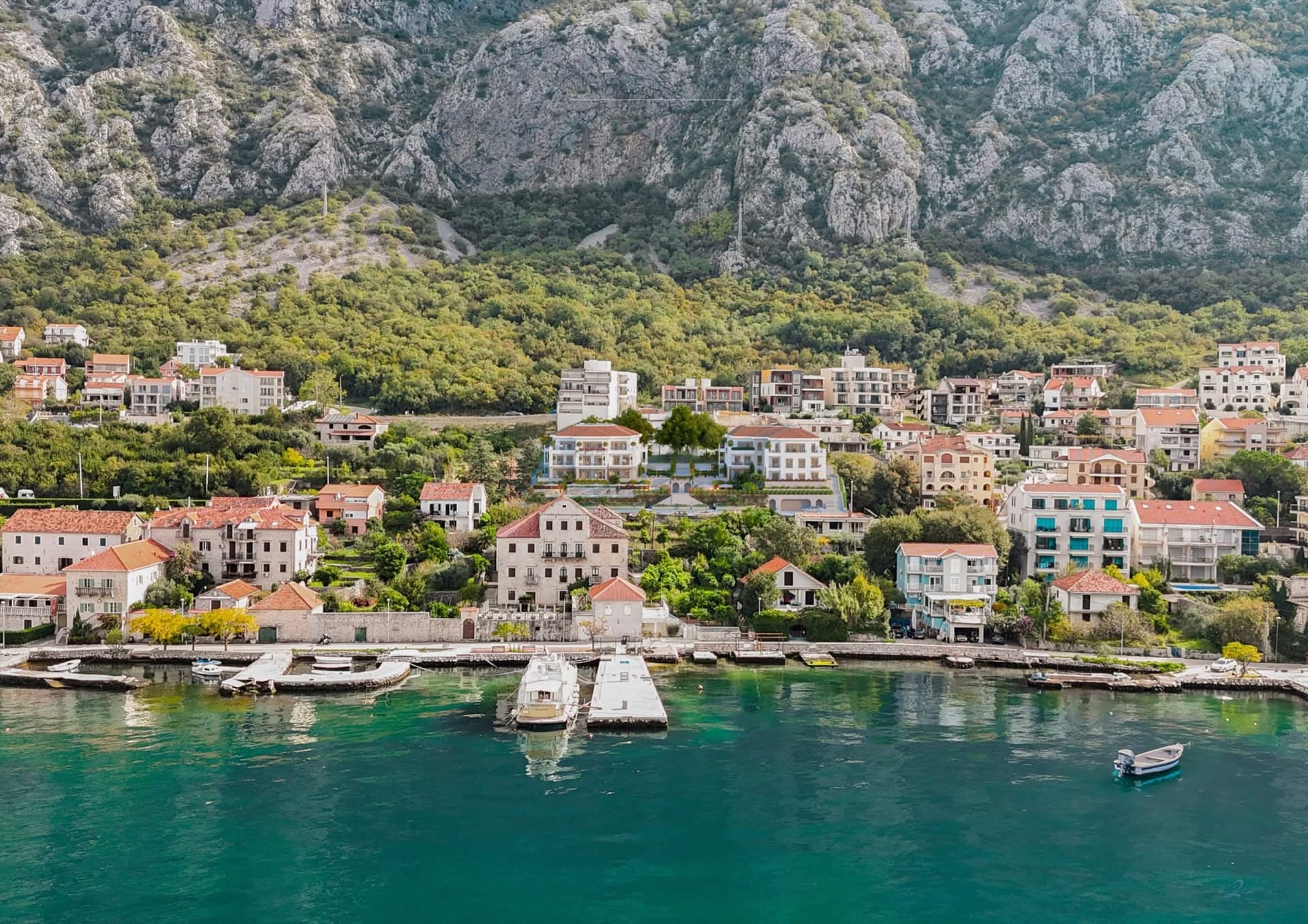 Sea view of a residential complex in Ljuta, Montenegro: coastal houses with tiled roofs, mountains, and a private pier.