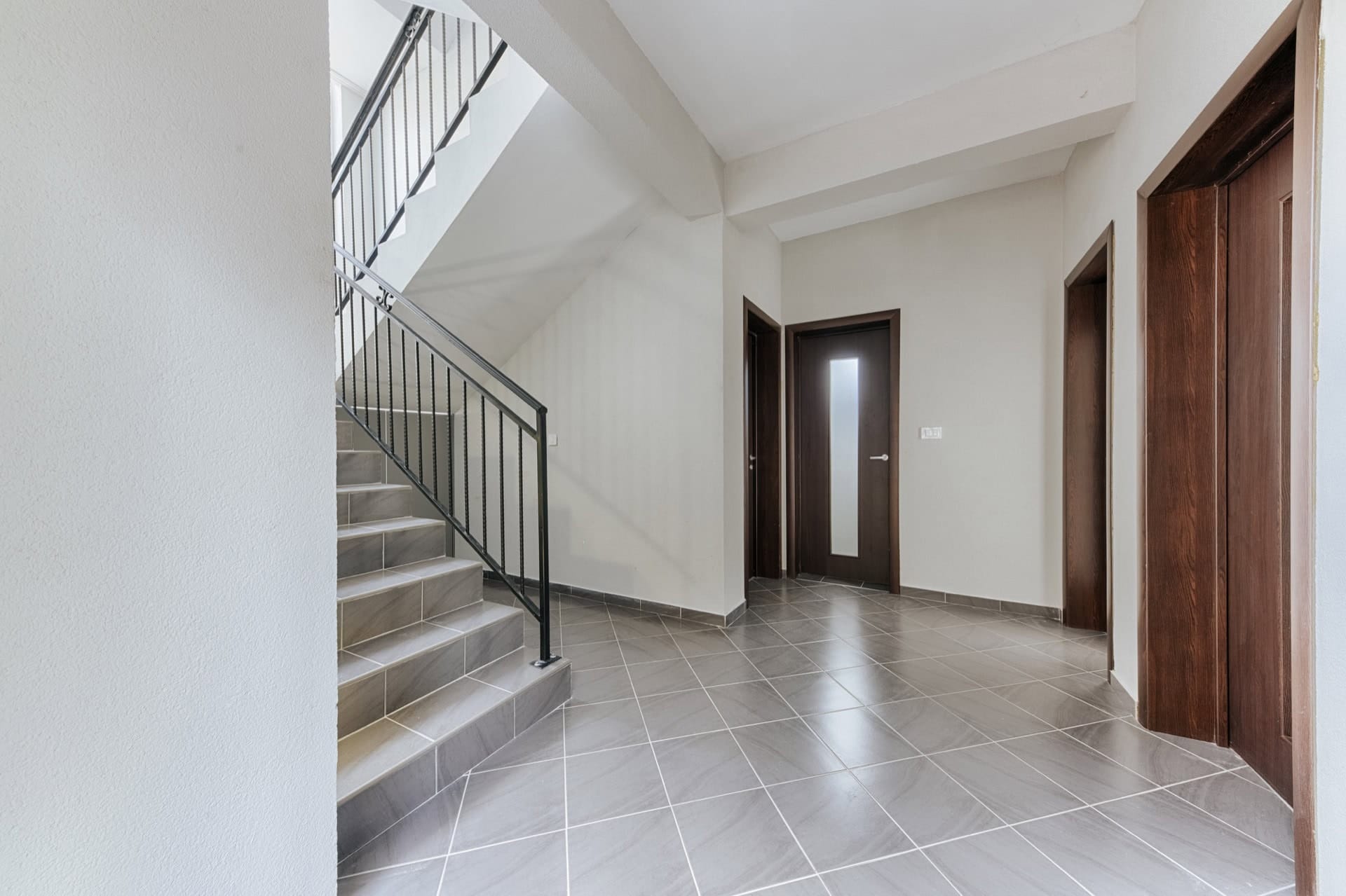 Bright hall with a staircase and dark interior doors in a villa in Utjeha, Montenegro. Modern tile finish.
