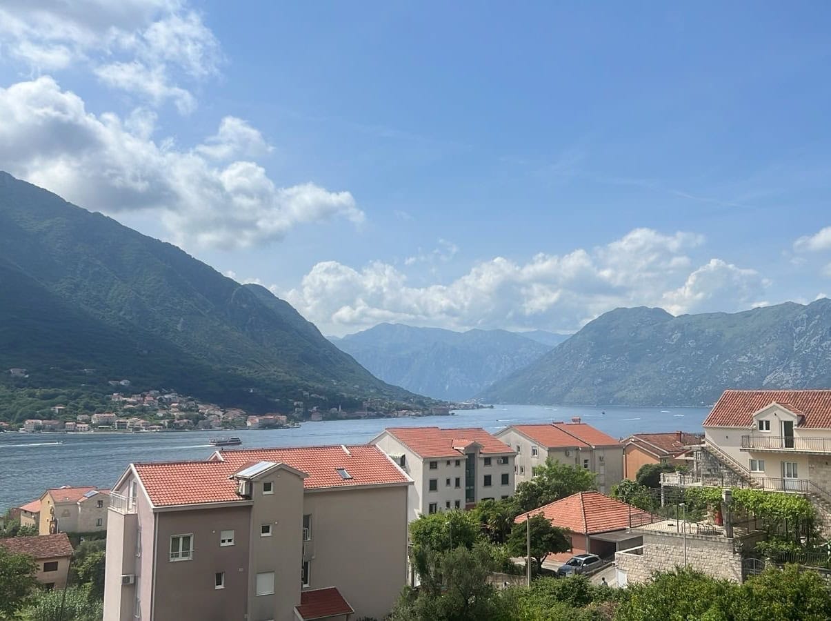 Panoramic view of the Bay of Kotor and mountains from an apartment in Dobrota, Montenegro: a residential area with tiled roofs.