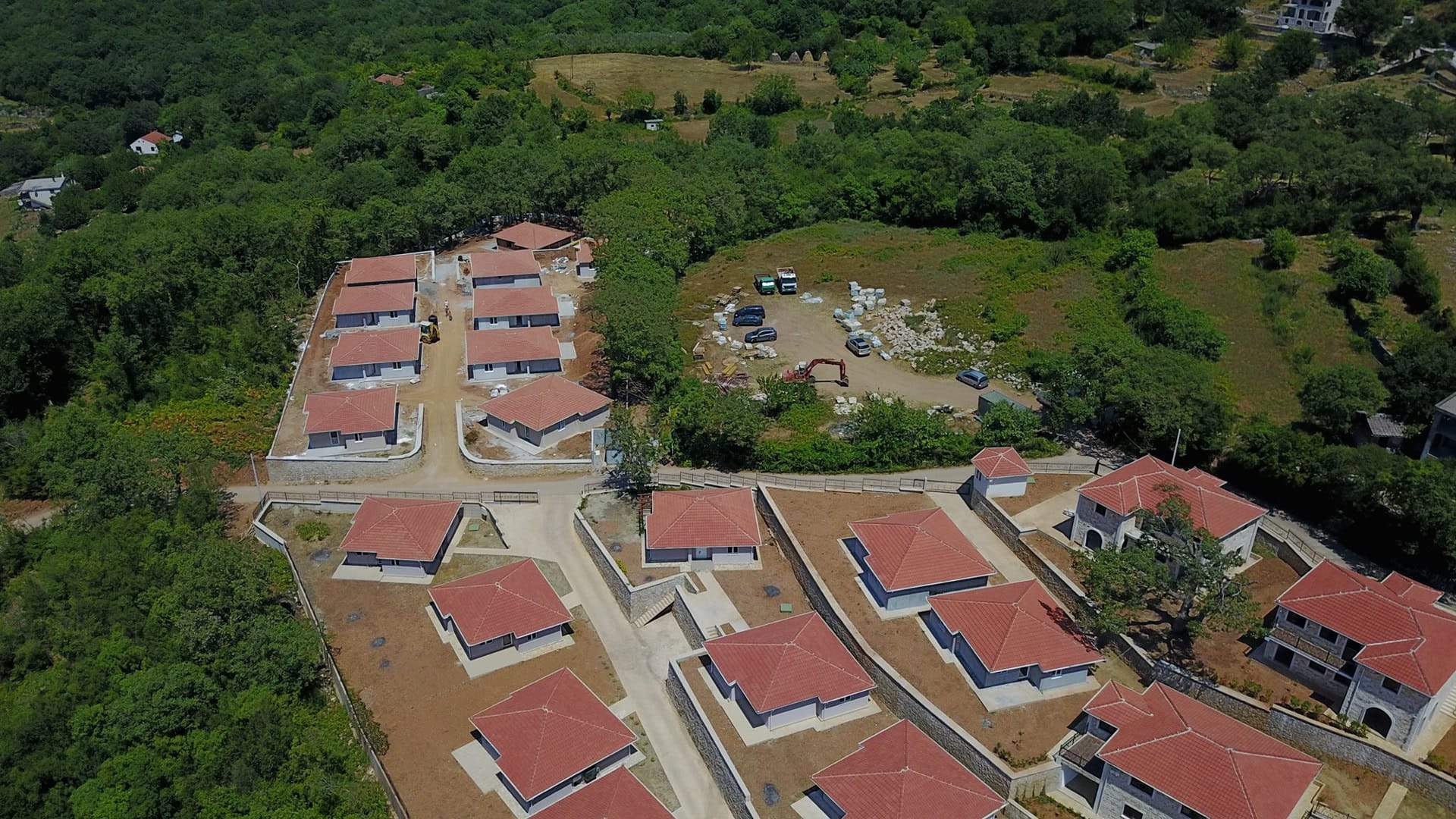 Aerial view of a cottage community under construction with red roofs surrounded by forest, Bar, Montenegro.