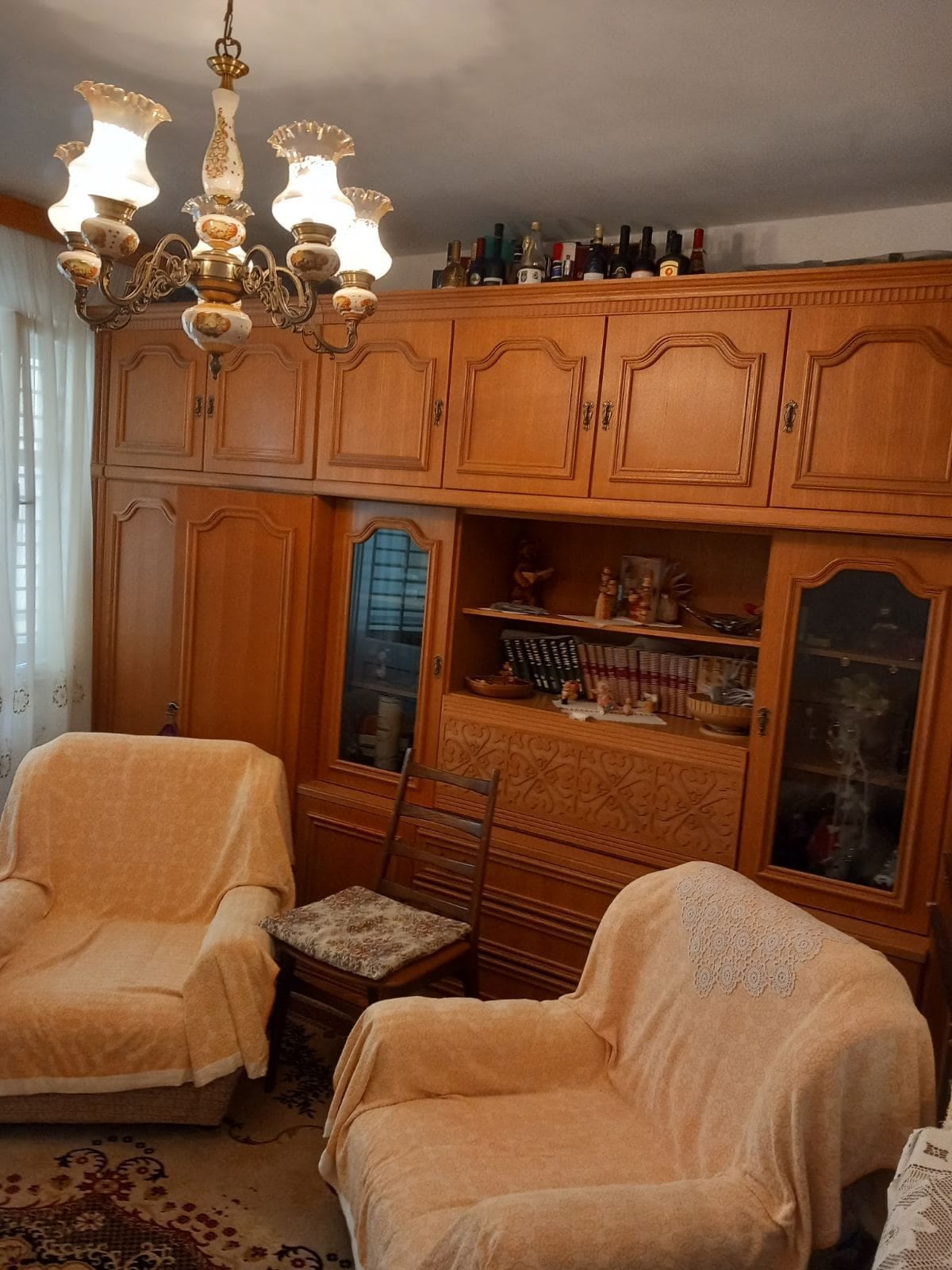 Living room in a house in Igalo, Montenegro: a classic wooden wall unit, upholstered armchairs, and a vintage chandelier in the interior.