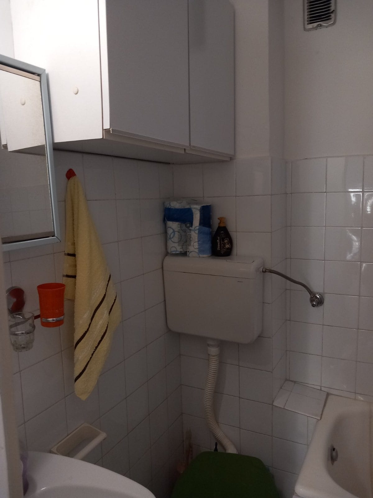 Bathroom in a house in Igalo, Montenegro: white tiles, wall cabinet, plumbing fixtures, and a mirror in the interior.