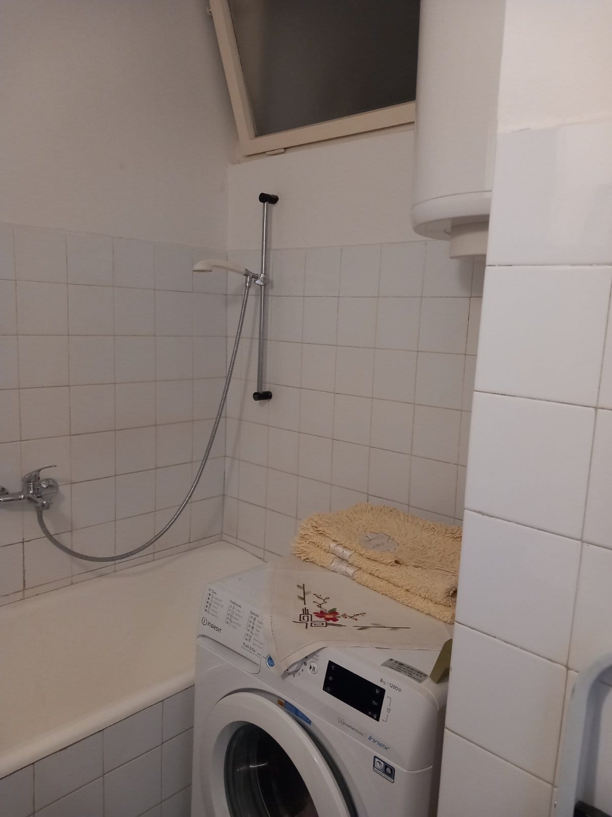 Bathroom in a house in Igalo, Montenegro: white tiles, bathtub, Indesit washing machine, and water heater.