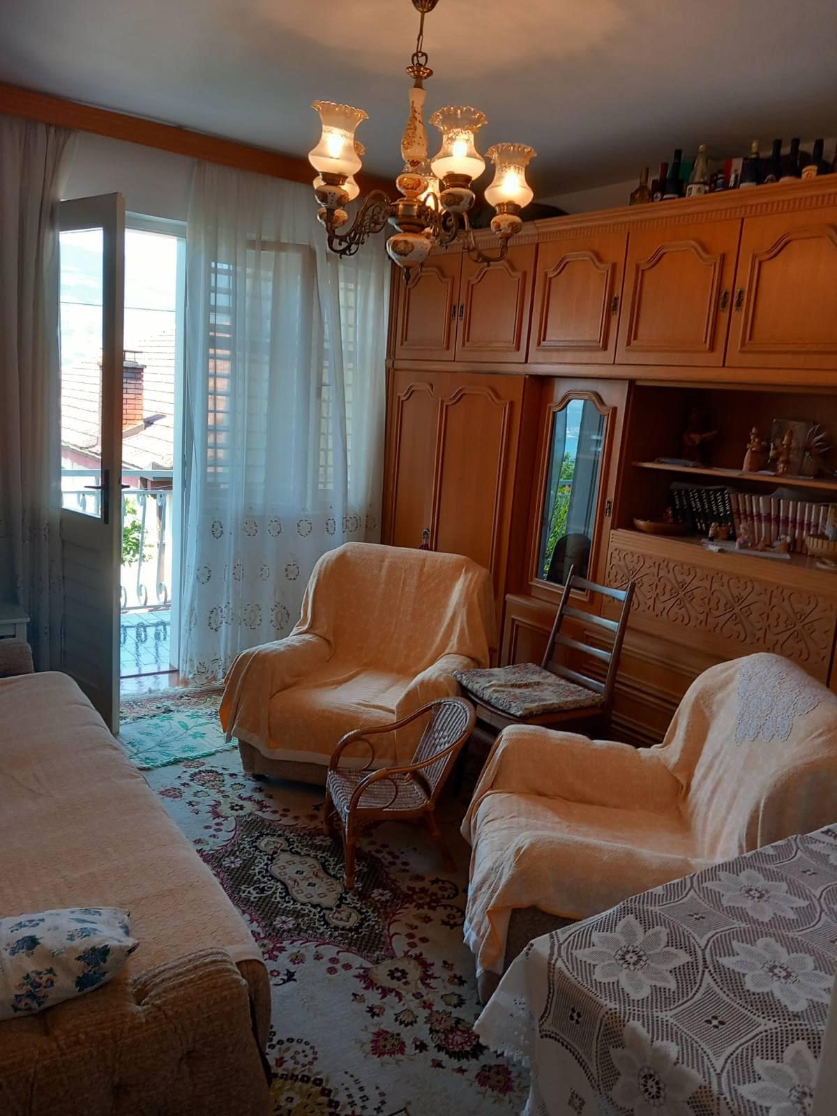 Living room in a house in Igalo, Montenegro: classic furniture, wooden set, carpet, and access to a balcony with a view.