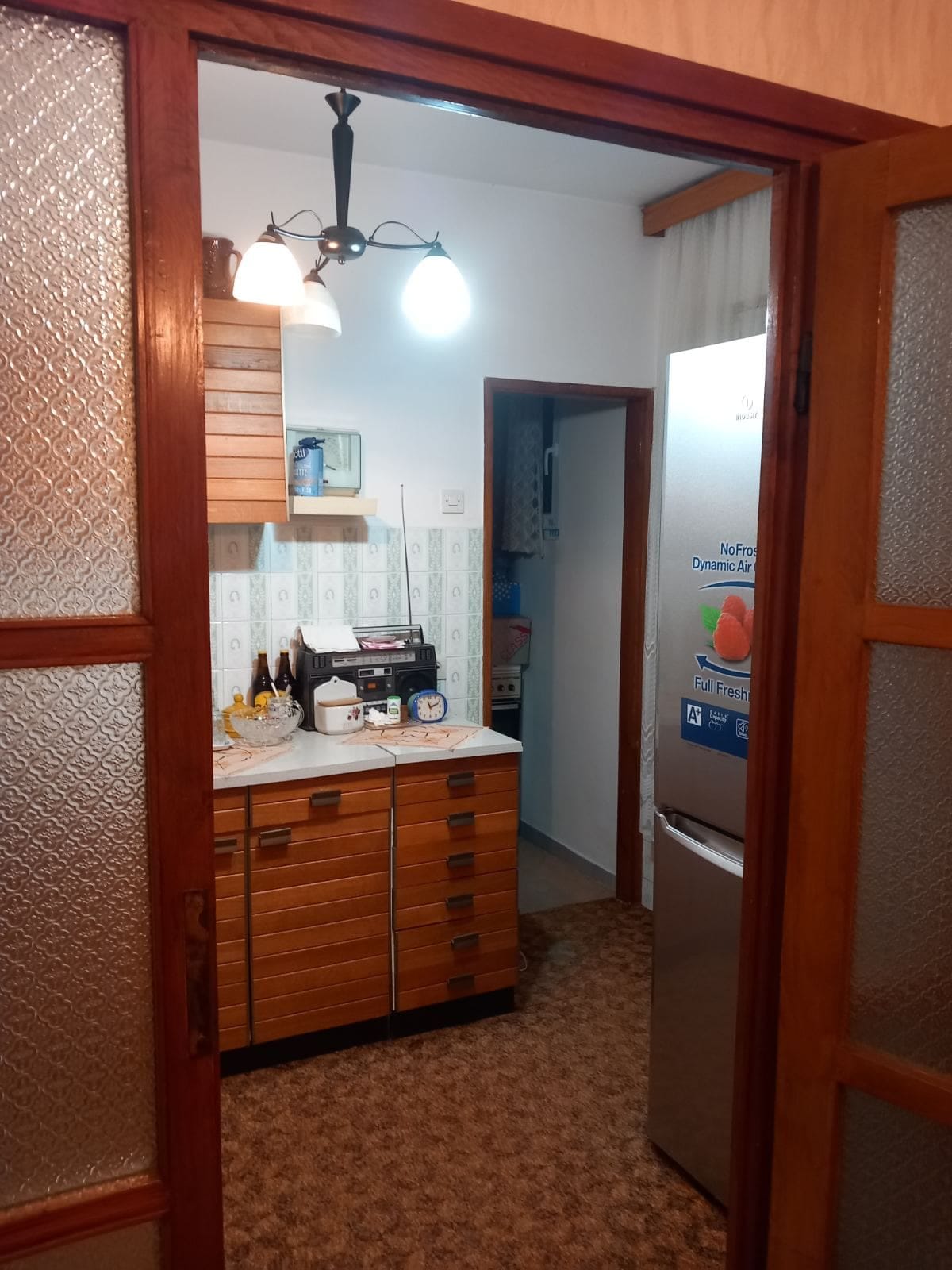 Kitchen with wooden cabinets and a refrigerator in a house for sale in Igalo, Montenegro. View through the doorway.