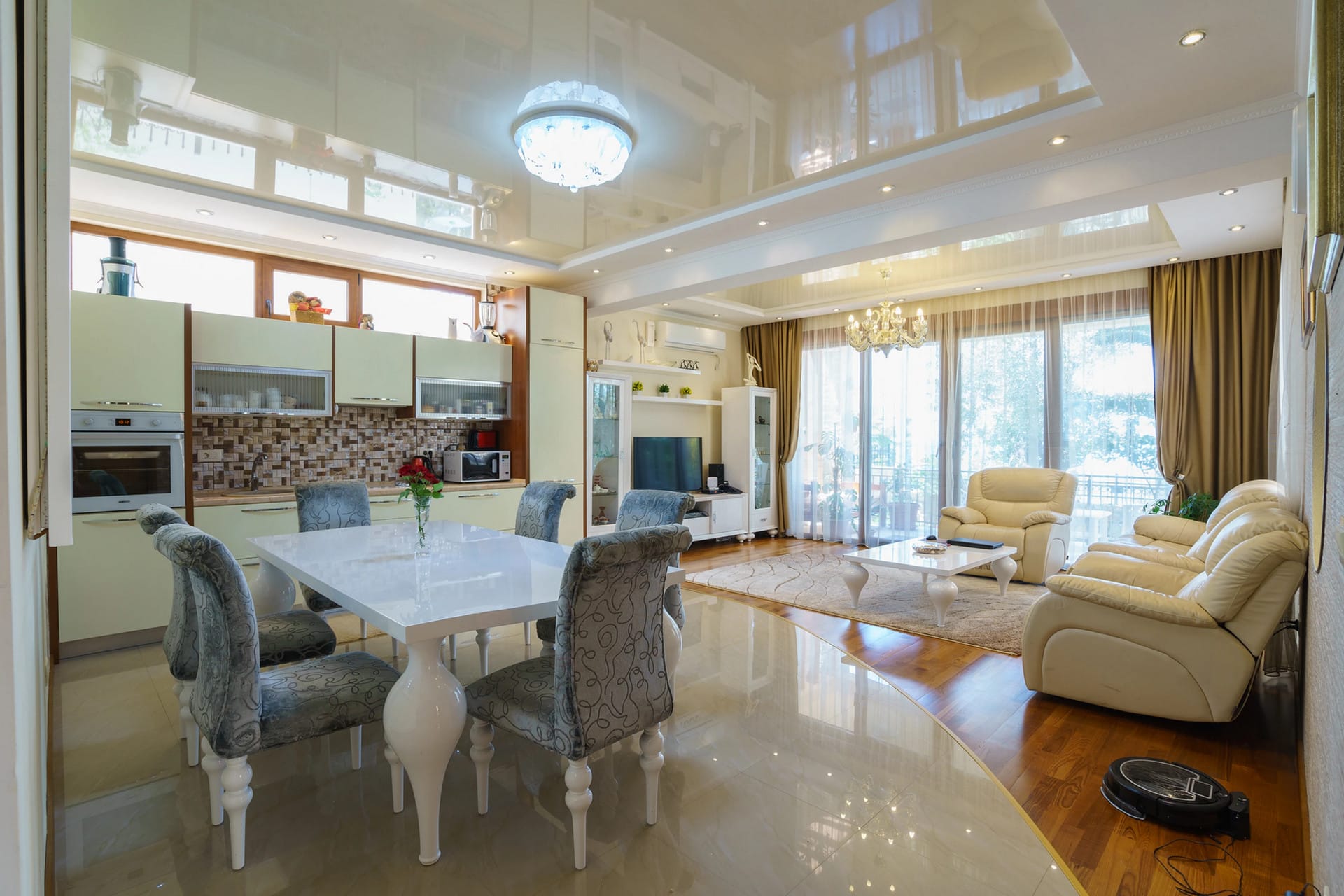 Spacious living room with kitchen in a house in Sutomore, Montenegro: light furniture, glossy ceiling, and panoramic windows.