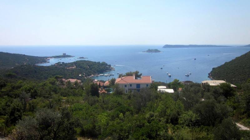 Panoramic view of the sea and Žanjice Bay, Montenegro, from a plot of land surrounded by greenery and Mediterranean mountains.