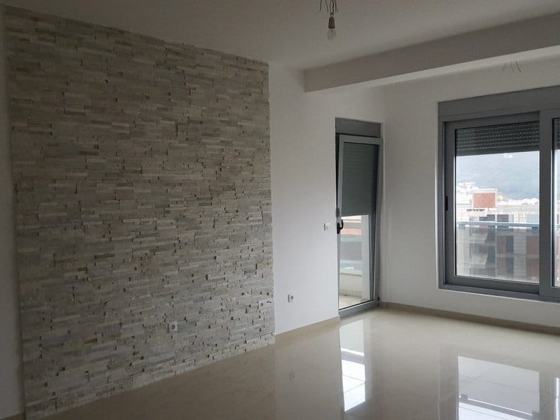 Bright living room in an apartment in Dobrota, Montenegro: an accent wall of decorative stone and access to the balcony.