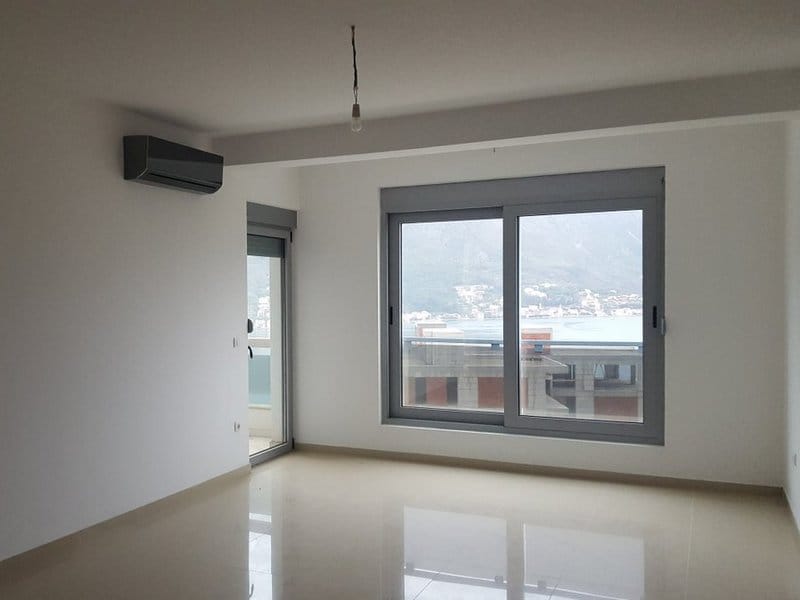 Bright living room in an apartment in Dobrota, Montenegro: panoramic windows with sea view, air conditioning, and tiled floor.