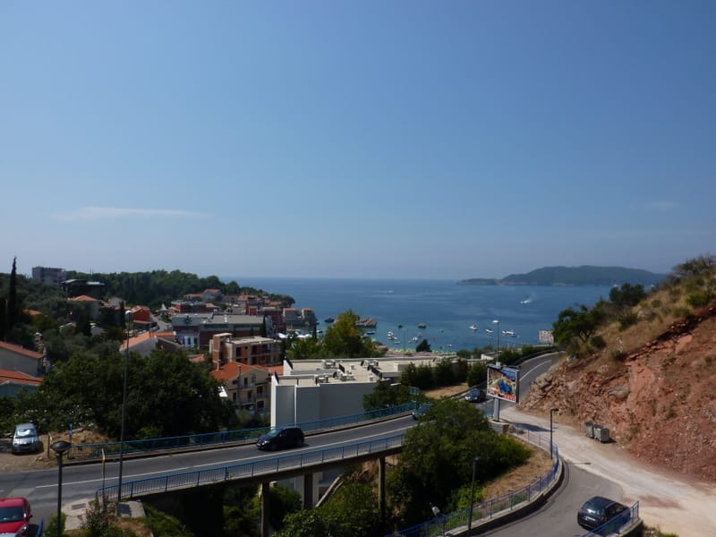 Panoramic view of the sea, bay, and the village of Pržno in Montenegro, with a road and green hills in the foreground