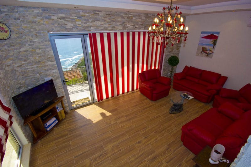 Living room with red furniture and sea view in a house in Dobra Voda, Montenegro: stone finishes and panoramic windows.