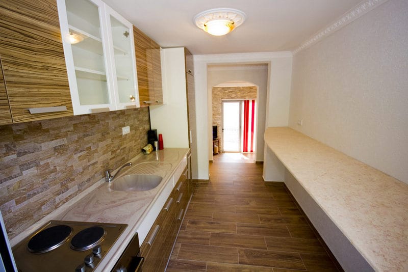 Modern kitchen in a house in Dobrih Voda, Montenegro: wood-finish cabinetry, stone backsplash, and a breakfast bar.