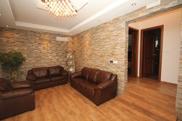 Living room in a house in Dobri Vody, Montenegro: leather sofas, decorative stone wall finish, and tiled floor.