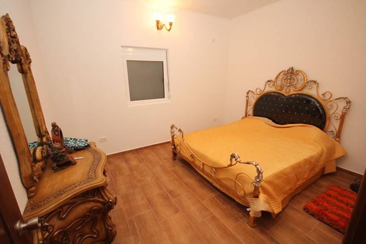 Bedroom with a wrought-iron bed and carved dresser in a house for sale, Dobri Vody, Montenegro. Bright interior with tile flooring.