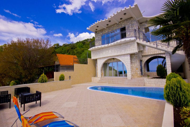 Two-story stone villa with a pool and terrace in Dobra Voda, Montenegro: view of the house with a lounge area and sun loungers.