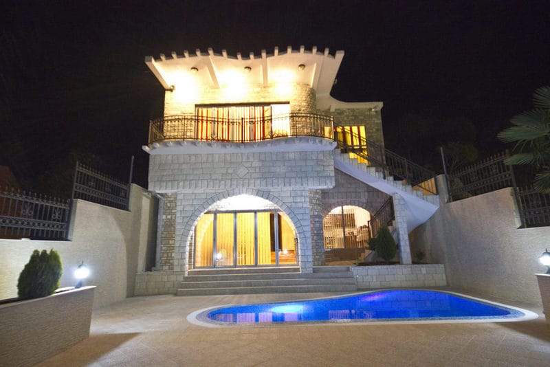 Two-story stone villa with a pool and lighting in Dobra Voda, Montenegro, front view of the house at night.