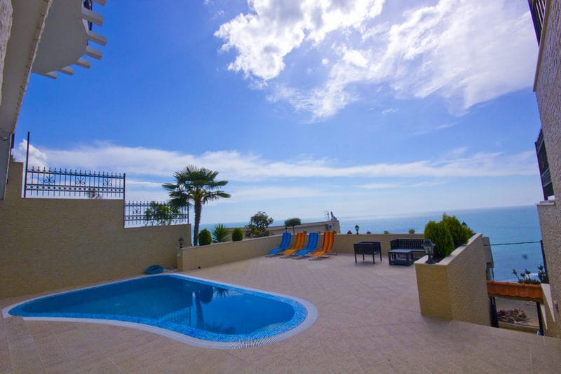 Terrace with a pool and sea view at a house in Dobri Vody, Montenegro: sun loungers, patio furniture, and a palm tree on the property.
