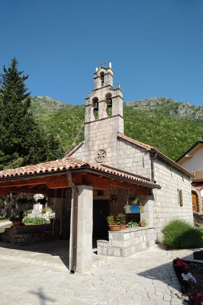 An old stone church near the property in Sveti Stefan, Montenegro, against a backdrop of green mountains and a clear sky.