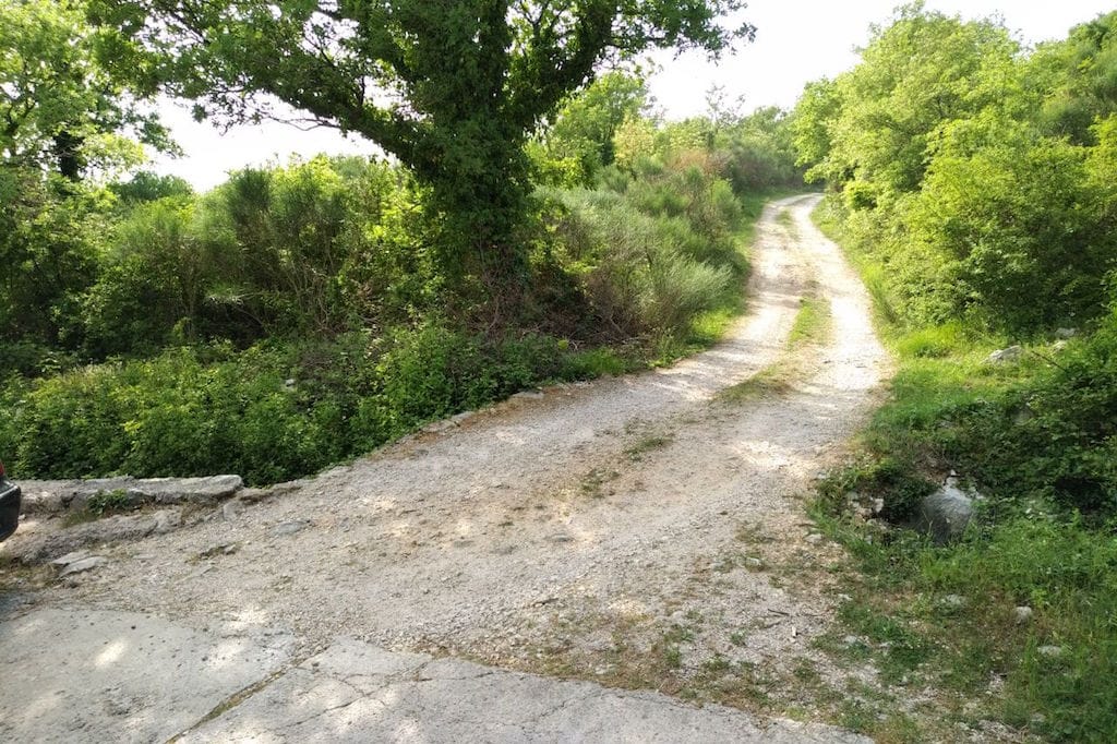 Dirt road to a land plot in Sveti Stefan, Montenegro, surrounded by green trees and shrubs.