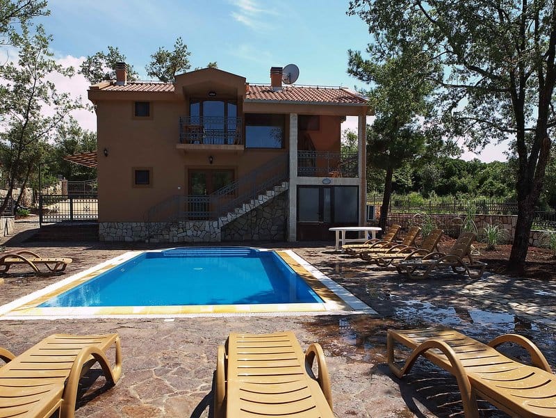 Two-story house with a pool and loungers in Krimovica, Montenegro: facade with a terrace and stone cladding.