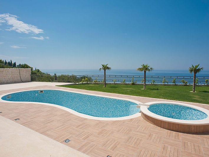 Open-air pool with jacuzzi and sea view at a villa in Reževići, Montenegro: tiled terrace and well-kept lawn.