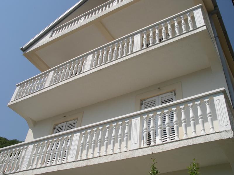 Three-story house in Baošići, Montenegro, with white balustrades on the balconies and classic facade detailing.