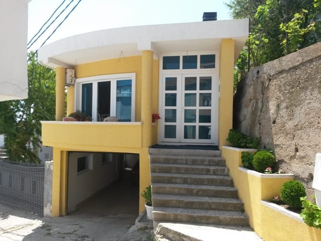 Yellow house in Ulcinj, Montenegro: facade with a terrace, panoramic windows, staircase, and an integrated garage on the ground floor.