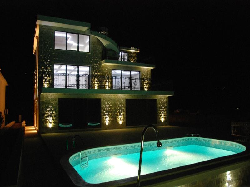 Three-story villa with a pool and nighttime facade lighting in Herceg Novi, Montenegro. Modern house with terraces.